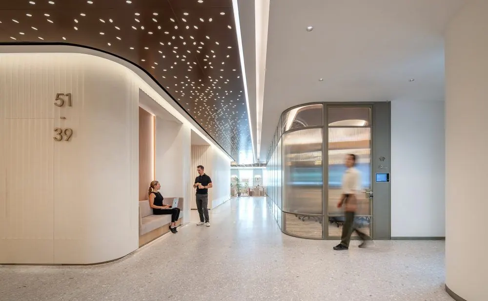 Curved corridor with a perforated ceiling and glass meeting pods